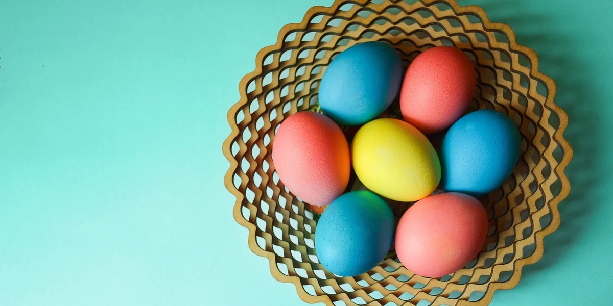 Colorful dyed eggs in a woven basket on a teal background.